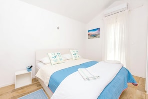 A bedroom with a bed, a nightstand, a window with curtains, and a wall-mounted air conditioner. - Apartments Mir (Dugi Rat)