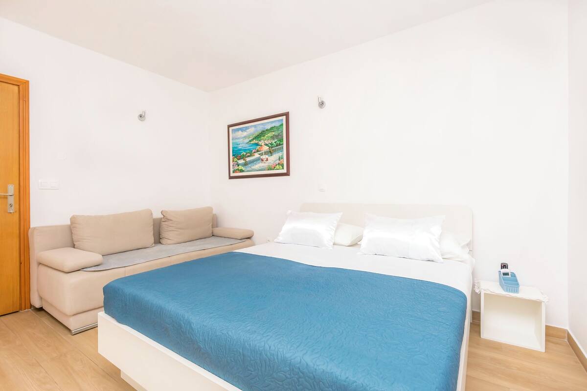 Une chambre à coucher avec un lit, un canapé, une table de chevet et un tableau encadré au mur.
