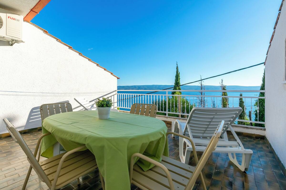 Un balcon avec une table et des chaises, une plante en pot et une vue sur la mer.
