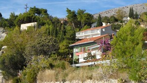 A hillside residential area with houses, dense greenery, and a rocky hill in the background. - Apartments Mari (Dugi Rat)