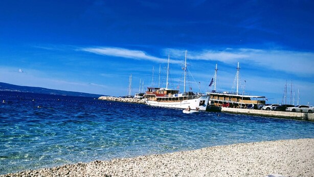 A marina with several sailboats docked, a pebbled beach, and a clear blue sky. - Apartments Mari (Dugi Rat)