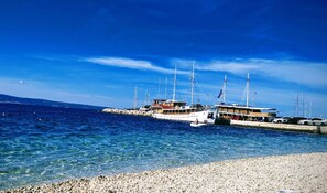 A marina with several sailboats docked, a pebbled beach, and a clear blue sky. - Apartments Mari (Dugi Rat)