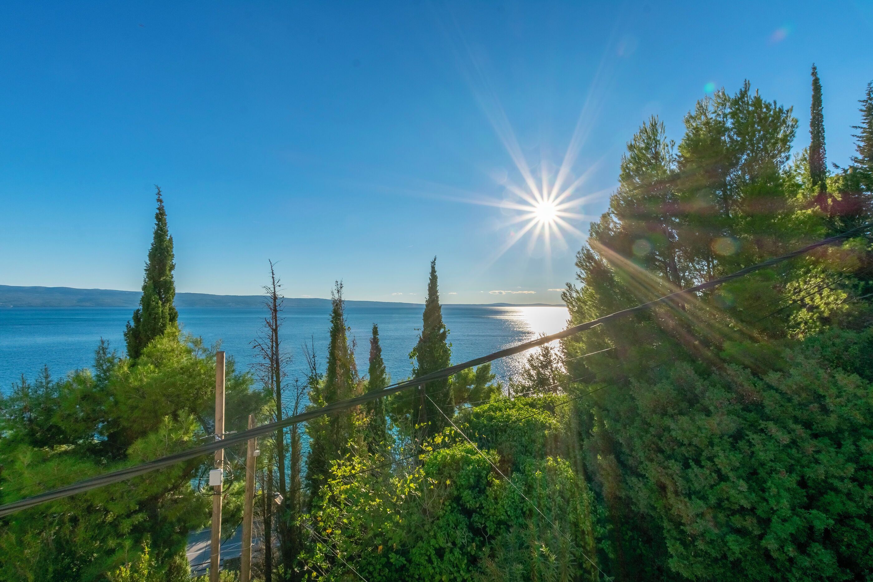 A scenic view of a coastal area with a clear sky, sun shining, and a body of water in the background.