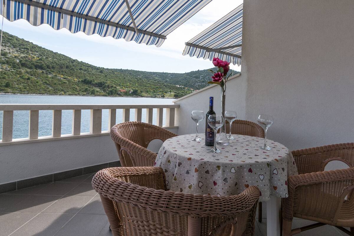 Un balcon avec des fauteuils en osier et une table, d’où l’on peut admirer un plan d’eau et des collines verdoyantes.