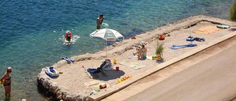 Una platja amb aigua cristal·lina, persones nedant i gandules i paraigües.