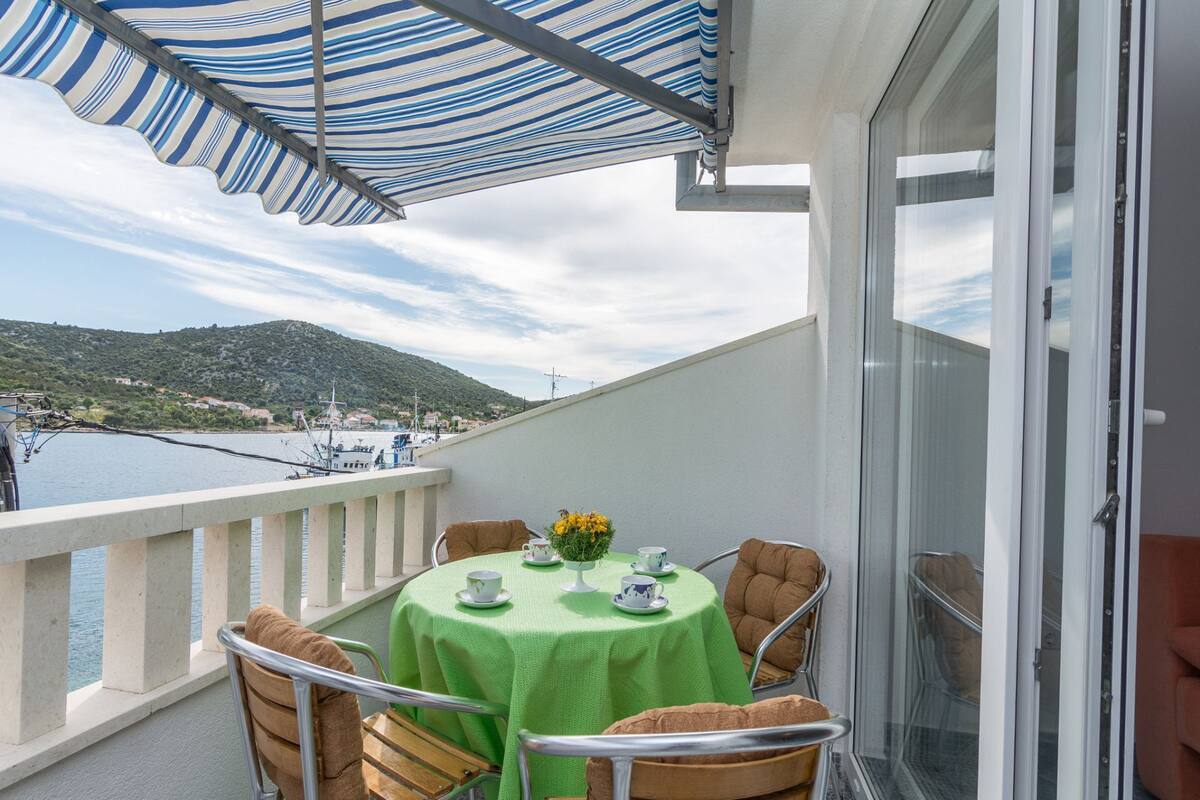 Un balcon avec une table verte, des chaises et un parasol à rayures.