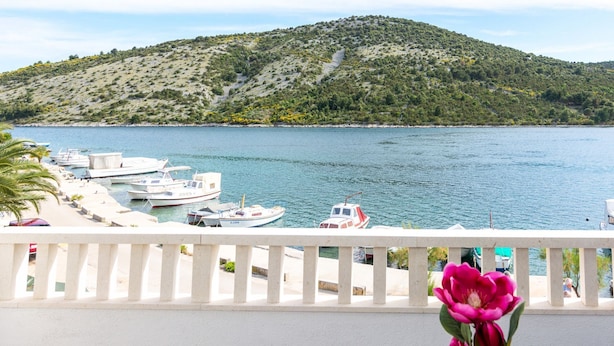 Ein Balkon mit Blick auf ein ruhiges Meer, wo Boote vor Anker liegen, und eine hügelige Landschaft.