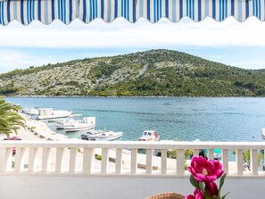 Un balcón con vistas al mar tranquilo, barcos amarrados y un paisaje montañoso.