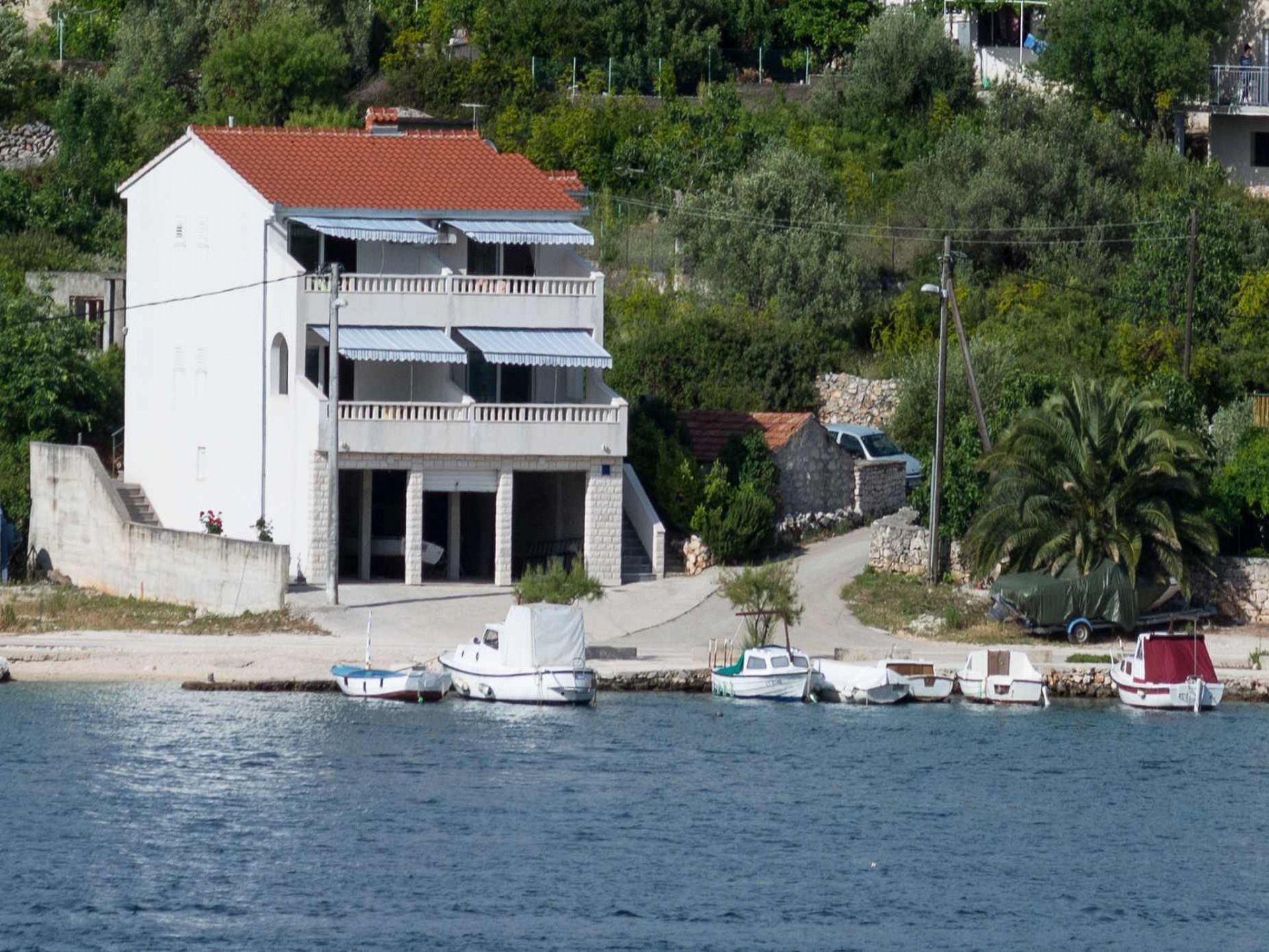 A white building with a red roof, a balcony, and a small boat docked in front.