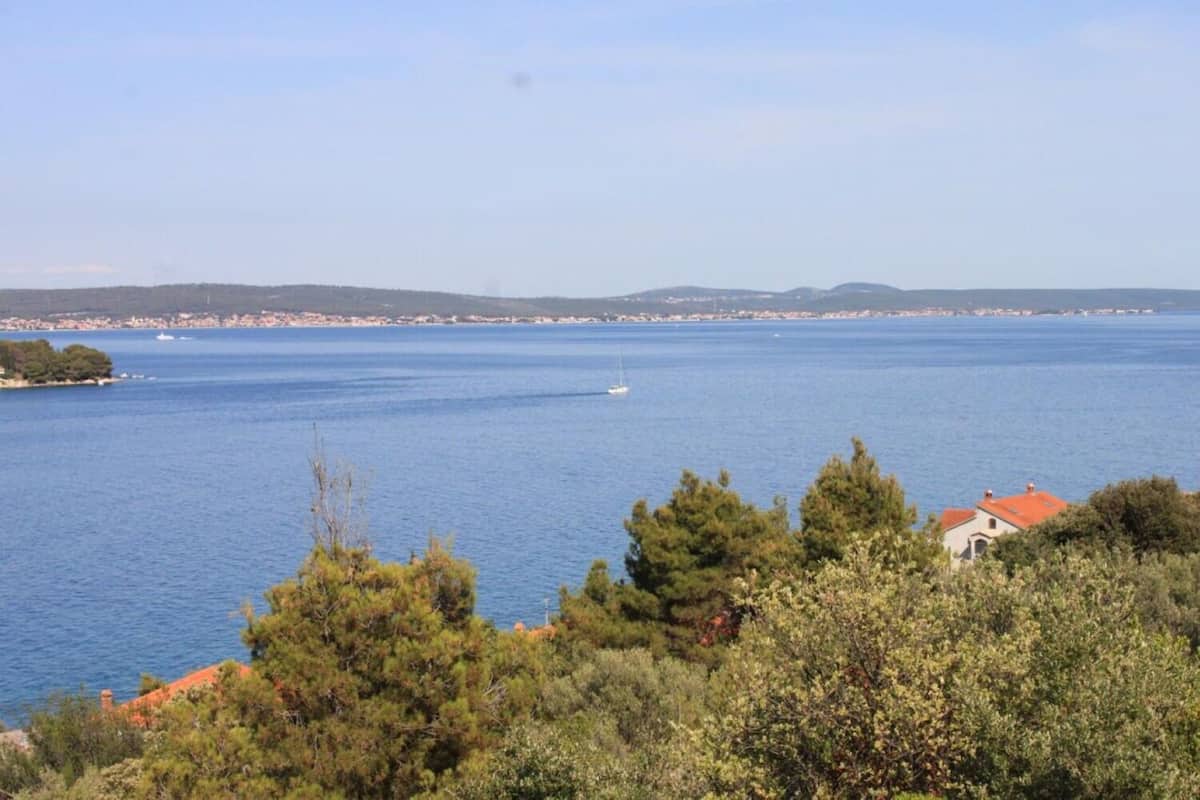 Blick auf die Küste mit blauem Meer, einem kleinen Boot und einer entfernten Uferlinie mit Gebäuden.