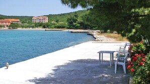 A waterfront patio with outdoor seating, a clear view of the sea, and a building in the background. - Apartment Ljube (Orebic)