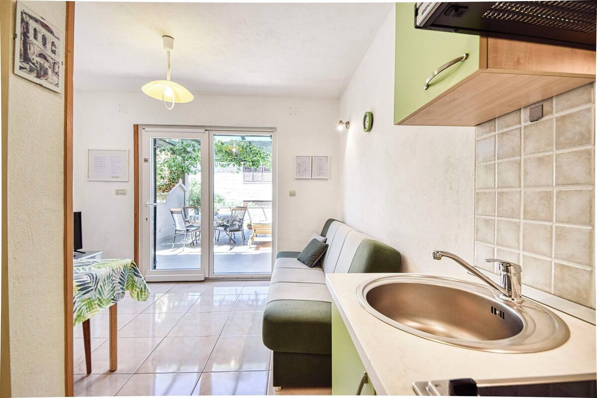 A compact kitchen with a sink, a dining area with a table and chairs, and a sliding glass door leading to an outdoor patio.