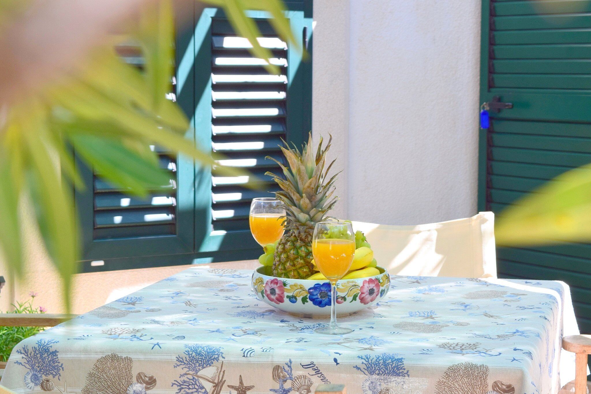 A table with a floral tablecloth, a bowl of fruit, and two glasses of orange juice.