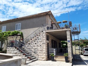 Ein zweistöckiges Gebäude mit einer Steinaußenwand, einem Balkon mit Pflanzen und einer Treppe zum Eingang.