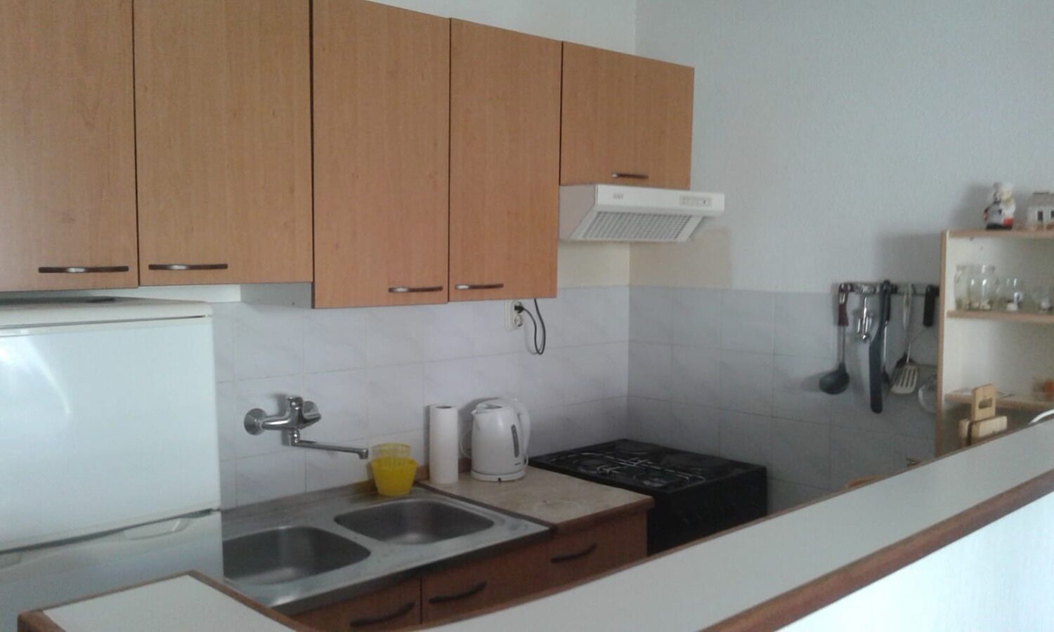 A compact kitchen with wooden cabinets, a white refrigerator, a stove, a sink, and a coffee maker.