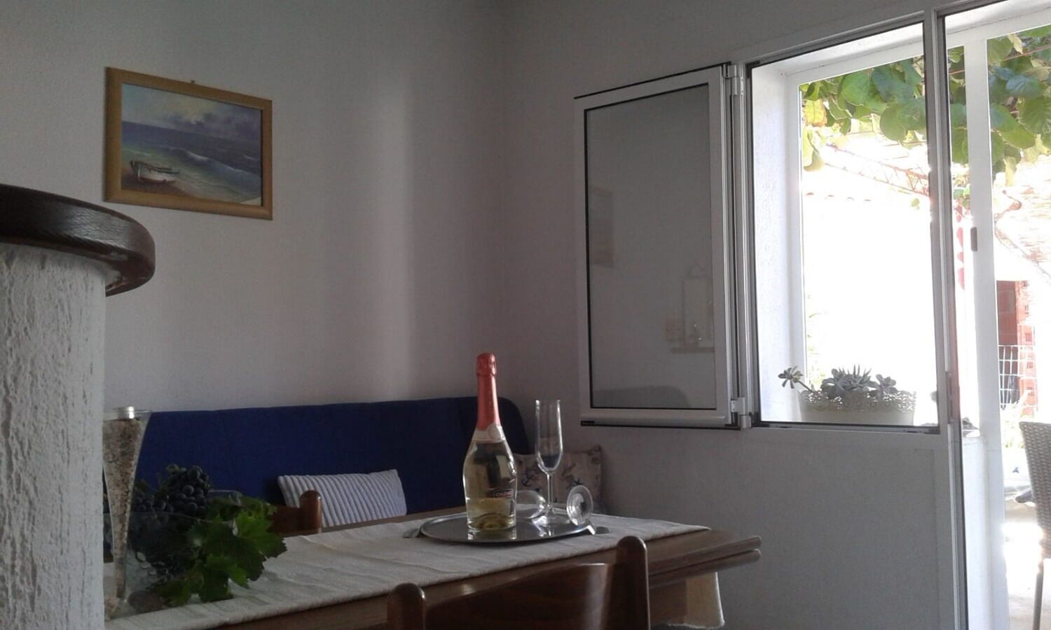Un comedor con una mesa lista para dos personas, una botella de vino y dos copas. Se ve un ventanal con vistas a follaje verde.