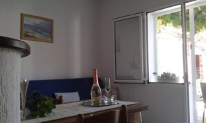 A dining area with a table set for two, a bottle of wine, and two glasses. There is a window with a view of greenery outside. - Apartments Marija (Supetar)