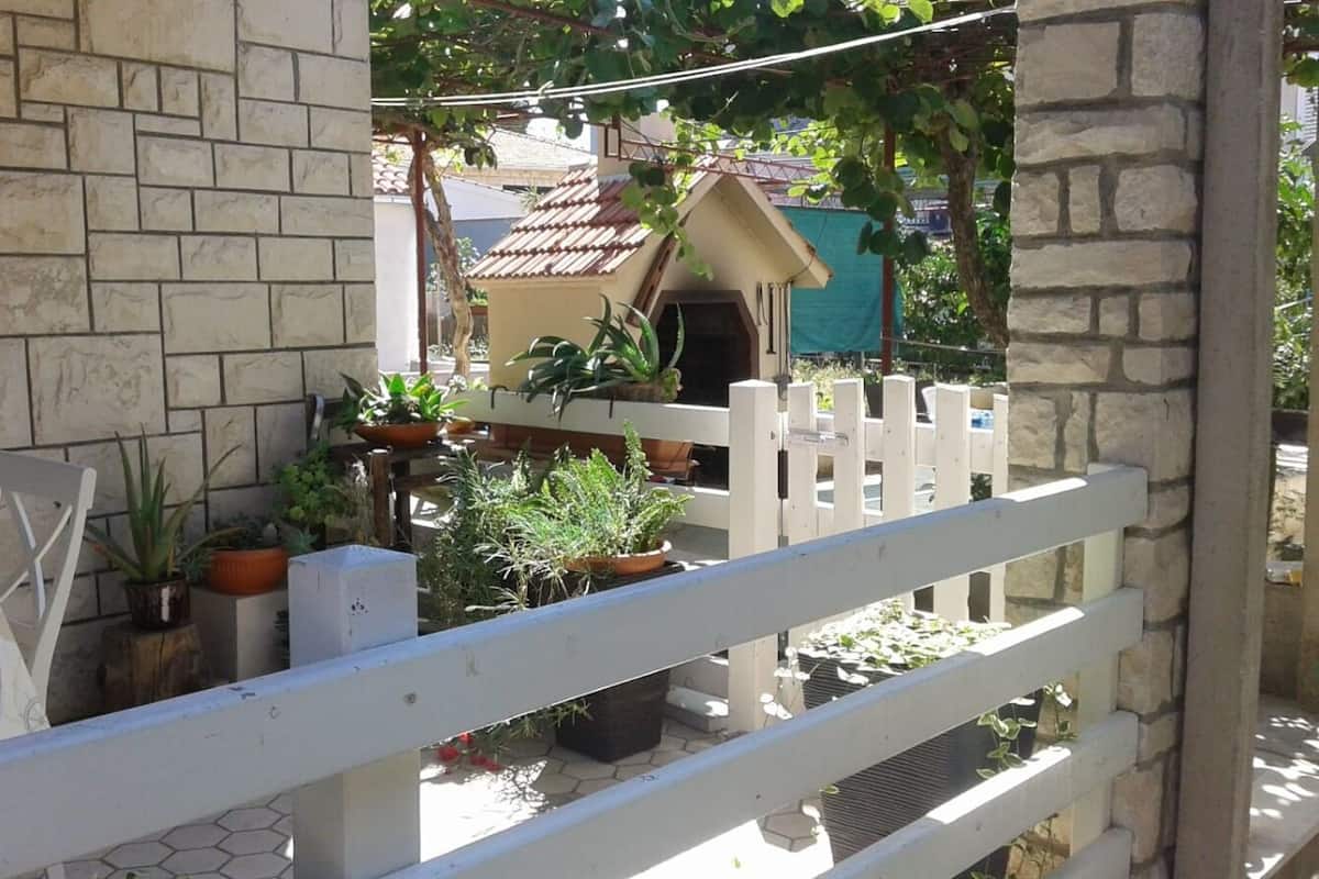 A balcony with a white fence, potted plants, and a view of a building with a tiled roof.
