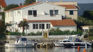 Een tweelaags huis met een rode pannendak, een balkon en een kleine boot die er afgemeerd ligt.