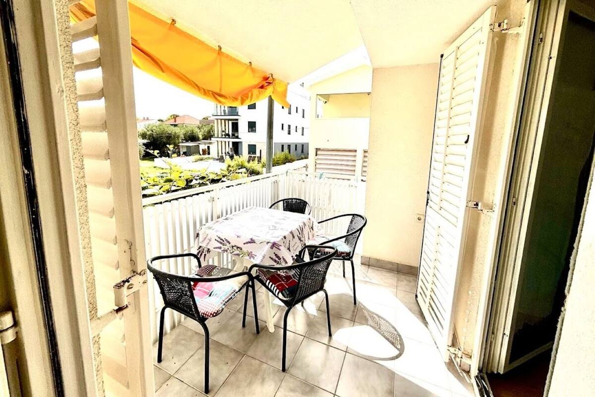 A balcony with a table and chairs, a yellow awning, and a view of buildings in the background.