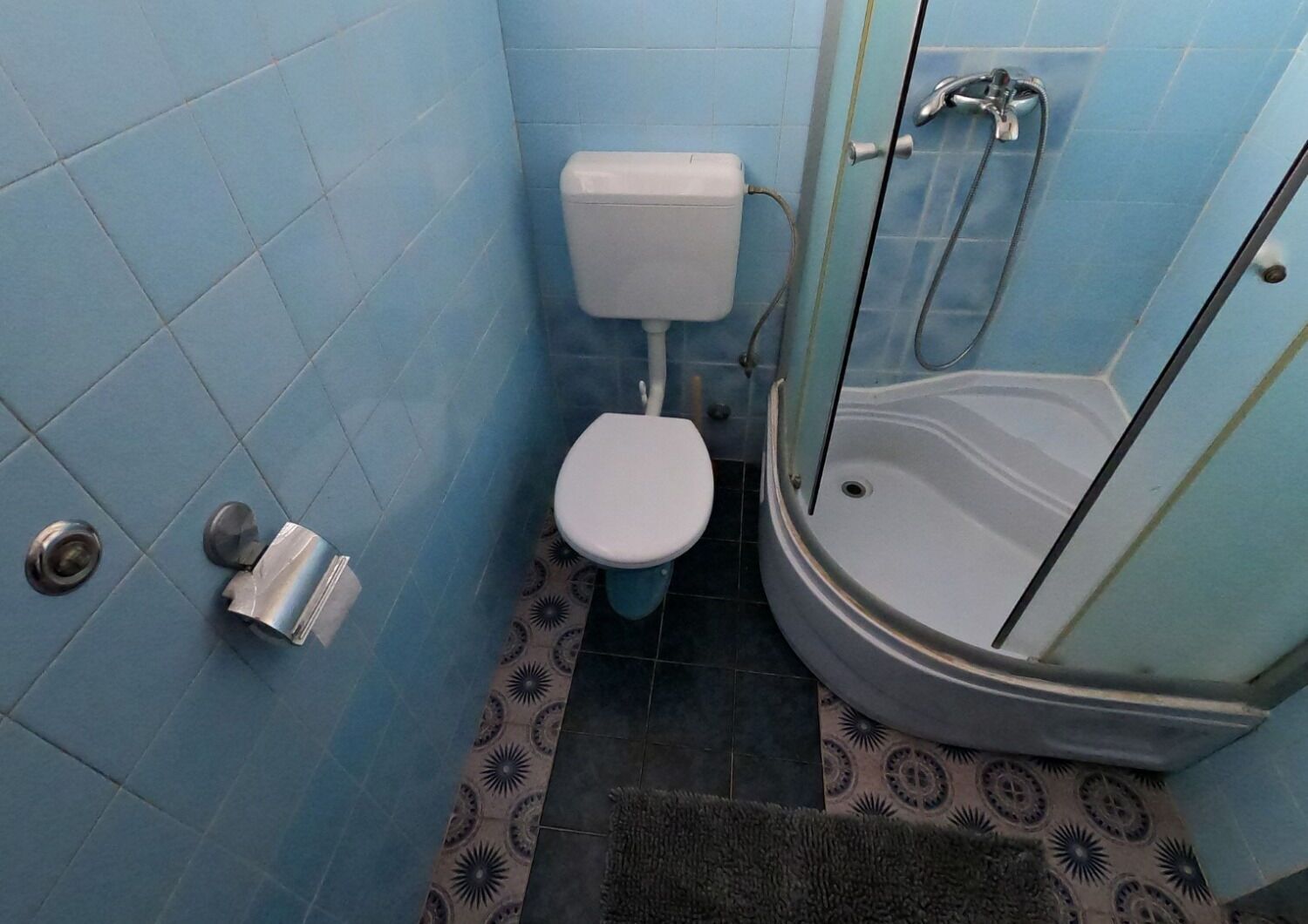 Kylpyhuone, jossa on wc, suihku ja kuviollinen lattia.
