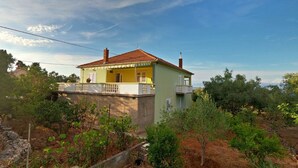 A two-story house with a balcony, surrounded by greenery and trees. - Apartment Mili (Preko)