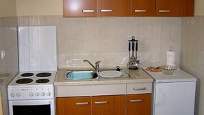 Una cocina con gabinetes de madera, estufa blanca, un lavamanos y un refrigerador pequeño.