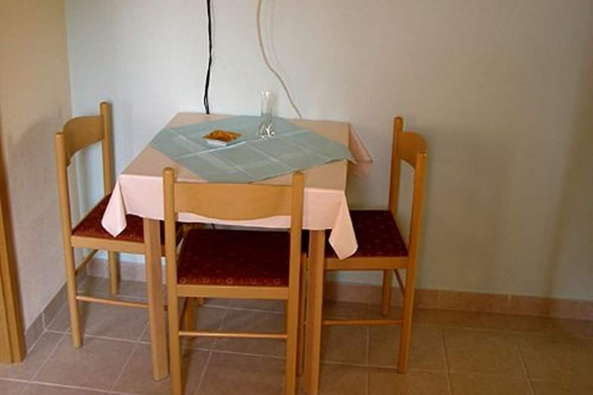 Una pequeña mesa de comedor con mantel, dos sillas y un vaso sobre la mesa.