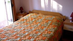 Una cama con colcha, una mesita de noche, una lámpara y una ventana.