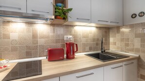 A modern kitchen with white cabinets, a wooden countertop, a red toaster, a red coffee maker, and a black induction cooktop. - Apartment Ljubav (Makarska)