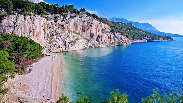 A coastal landscape with a rocky cliff, clear blue sea, and a pebble beach. - Apartment Ljubav (Makarska)
