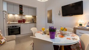 A compact kitchen with modern appliances, a dining area with a table set for two, and a flat-screen TV mounted on the wall. - Apartment Ljubav (Makarska)