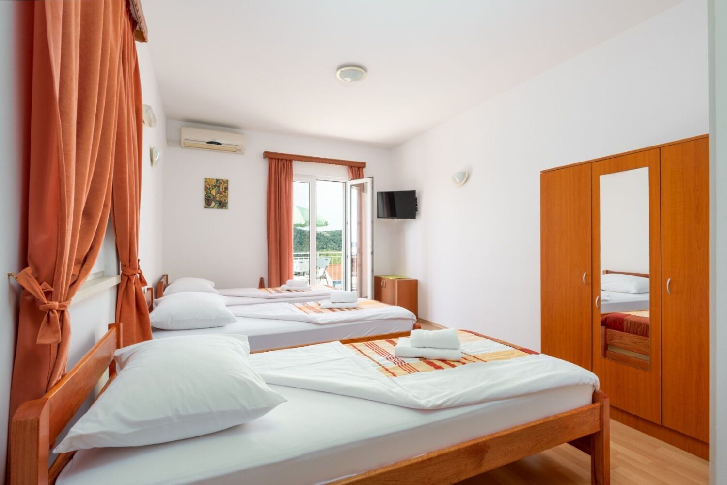 A hotel room with two single beds, a wooden wardrobe, a television, and a large window with curtains.