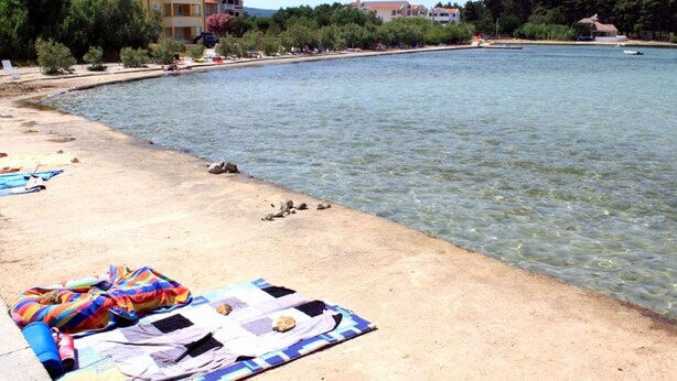 A beach with clear water, a sandy shore, and buildings in the background. - Apartments Den (Pasman)