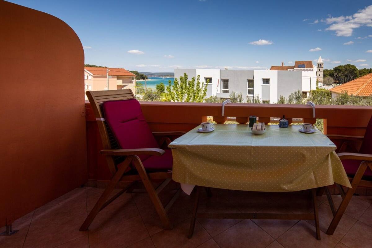 A balcony with a table set for two, chairs, and a view of buildings and a body of water.