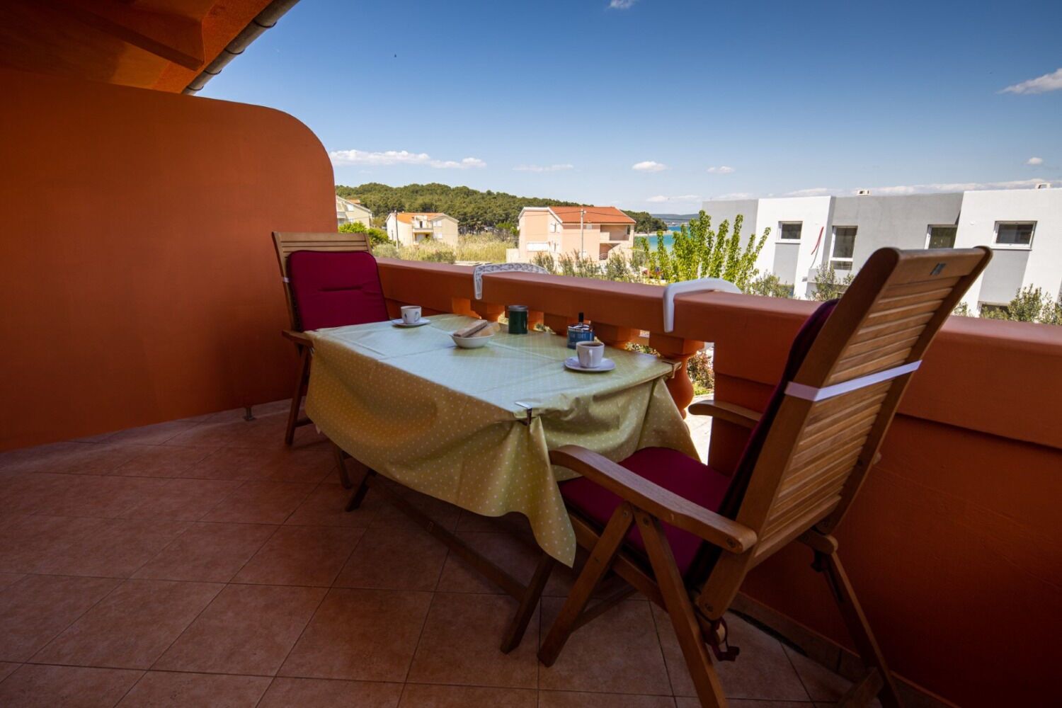 Une terrasse avec une table et des chaises, d’où l’on peut admirer des bâtiments et de la verdure en arrière-plan.