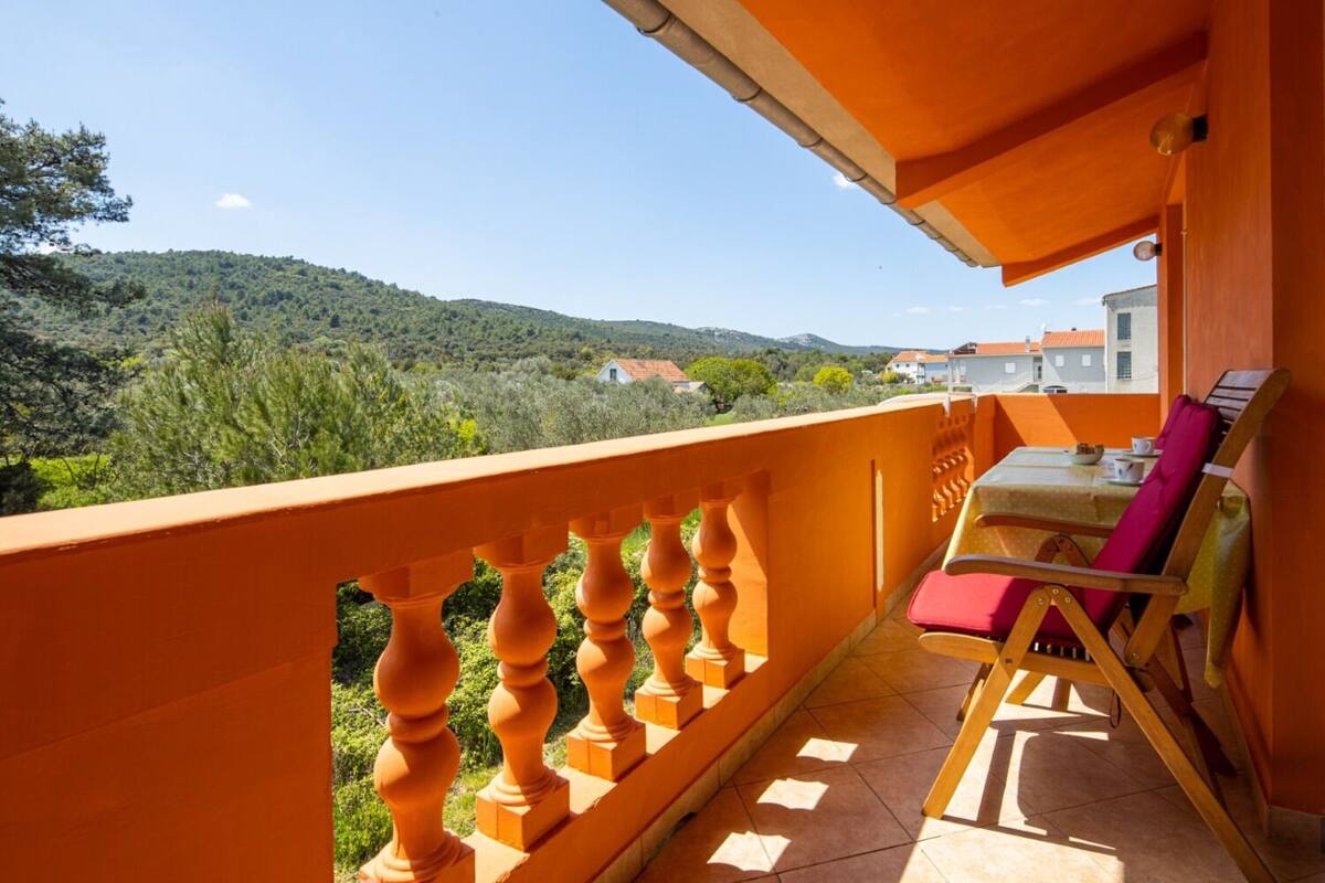 A balcony with a view of a hilly landscape, a table with chairs, and a tiled floor.