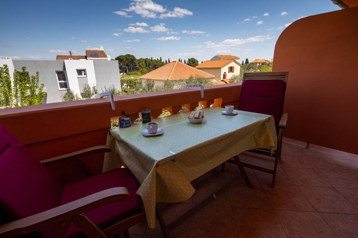 A balcony with a table set for two, chairs, and a view of buildings and trees.