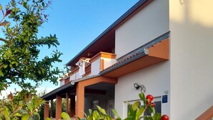 A two-story building with a white facade and orange accents, featuring a covered porch and a staircase with white balusters. - Apartments Den (Pasman)