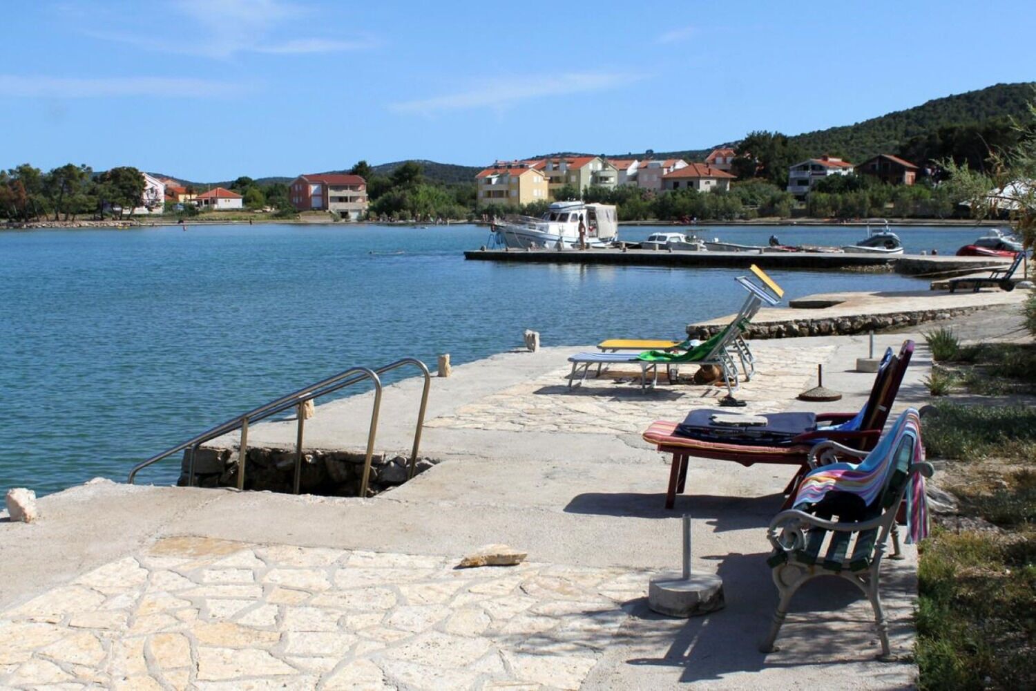 A waterfront dock with a stone walkway, lounge chairs, and a small table.