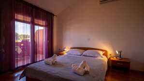 A bedroom with a bed, two bedside tables with lamps, a window with curtains, and a view of the outdoors. - Apartments Den (Pasman)