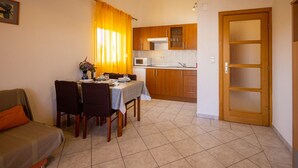 A compact living space with a dining area, kitchenette, and a sofa. - Apartments Den (Pasman)