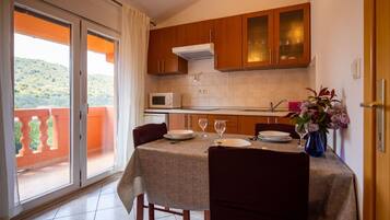 A dining area with a table set for two, a microwave, and a sink in the kitchen.