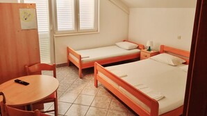 A small, single-room hotel with two wooden beds, a small table, and a chair. - Apartment Vido (Trpanj)