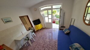 A room with a blue sofa, a small table with a yellow cloth, a TV on the wall, and a door leading outside. - Apartment Vido (Trpanj)
