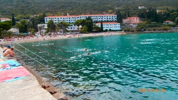 A coastal hotel with a swimming pool, beach, and mountainous backdrop. - Apartment Vido (Trpanj)