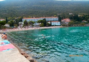 A coastal hotel with a swimming pool, beach, and mountainous backdrop. - Apartment Vido (Trpanj)