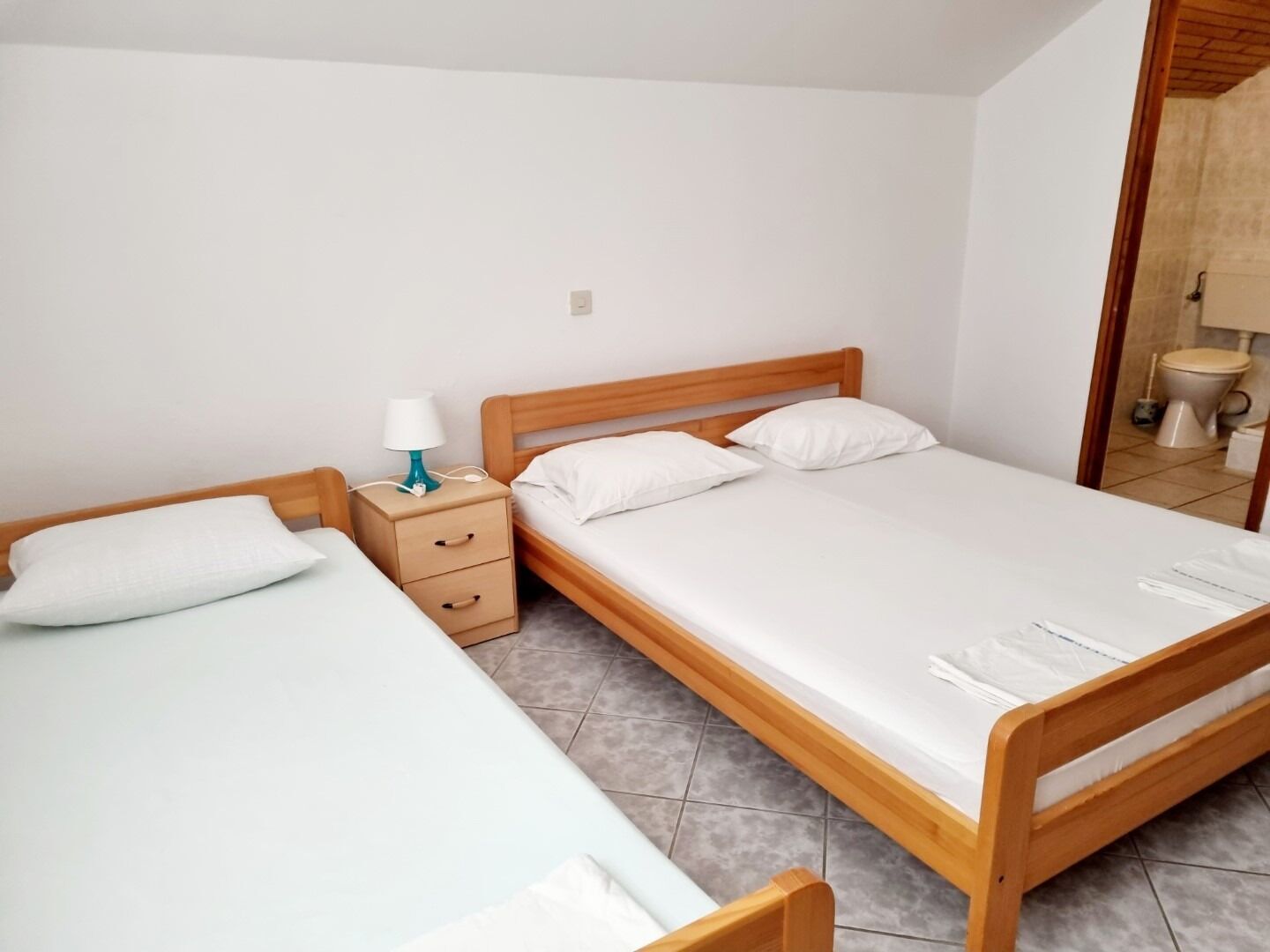 A bedroom with a wooden bed, a nightstand with a lamp, and a bathroom visible through an open door.
