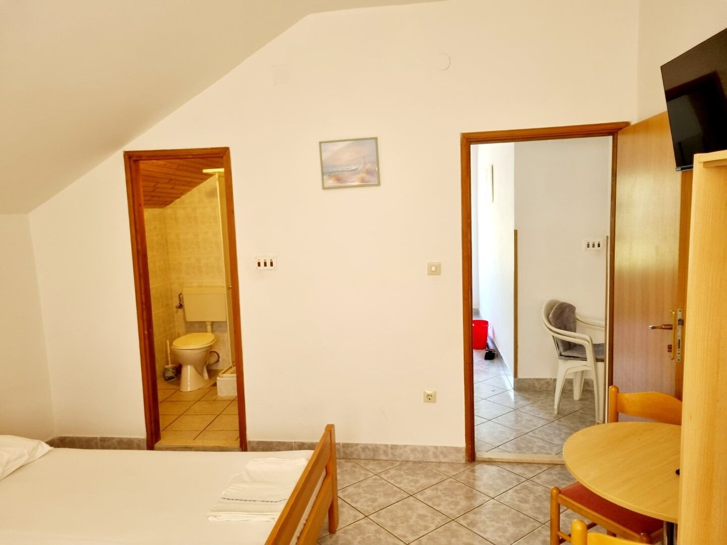 A bedroom with a bed, a wooden door leading to a bathroom, and a small table with a chair.