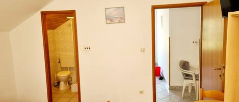 A bedroom with a bed, a wooden door leading to a bathroom, and a small table with a chair.